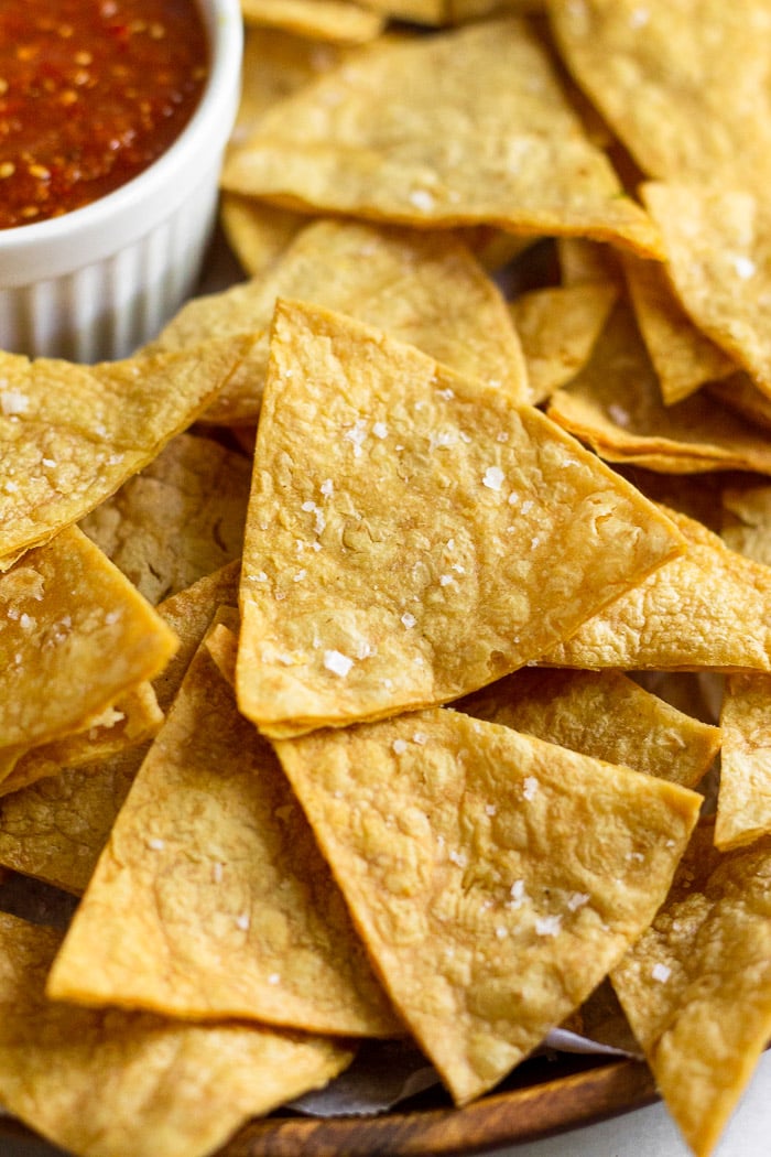 Close up of homemade tortilla chips with salt. In the background is a container of salsa.
