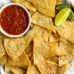 Overhead shot of a plate of air fryer tortilla chips with a small bowl of salsa and 2 lime wedges.