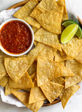 Overhead shot of a plate of air fryer tortilla chips with a small bowl of salsa and 2 lime wedges.