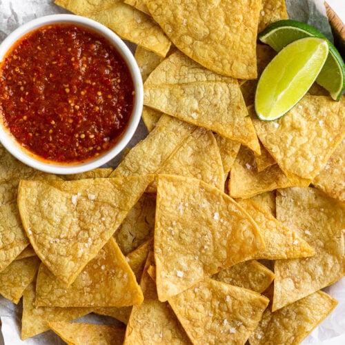 Overhead shot of a plate of air fryer tortilla chips with a small bowl of salsa and 2 lime wedges.