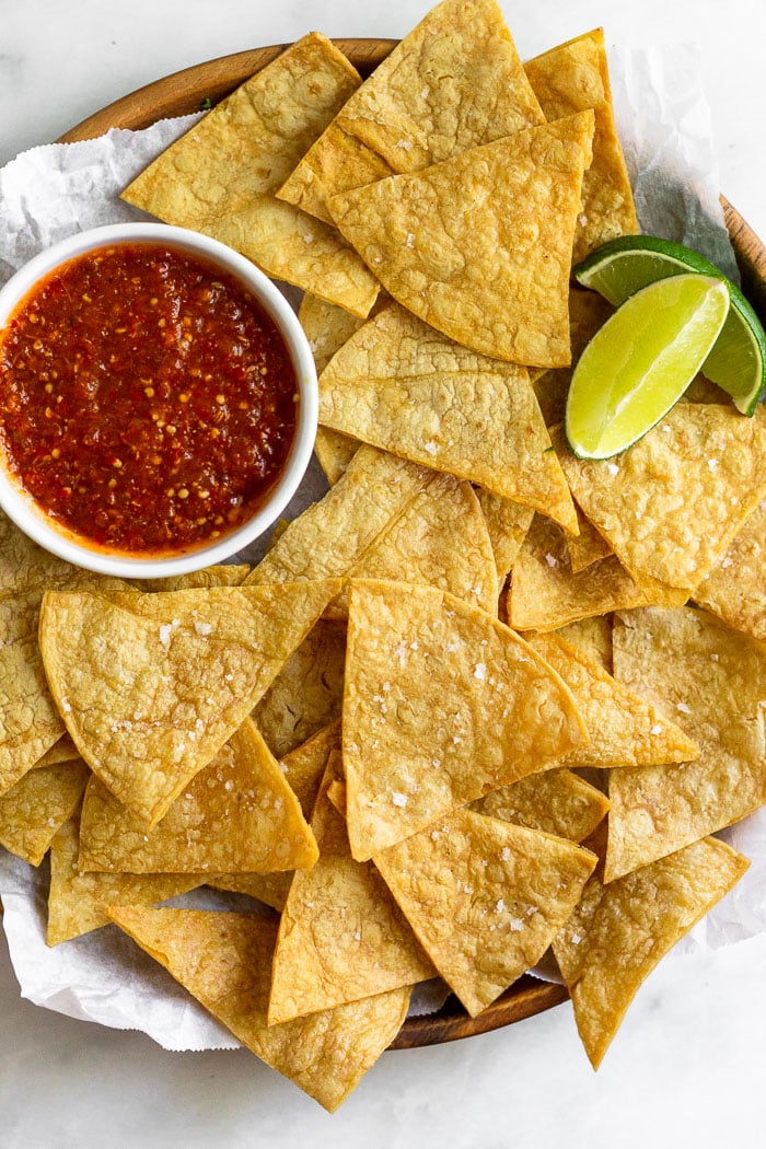 Overhead shot of a plate of air fryer tortilla chips with a small bowl of salsa and 2 lime wedges.