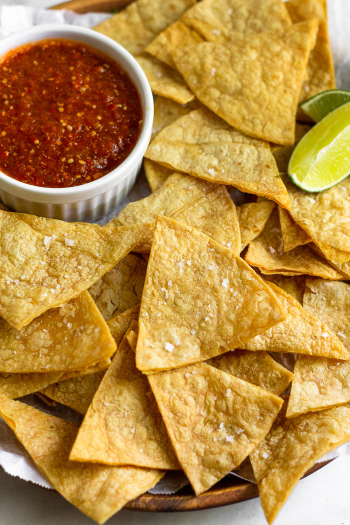 Plate of homemade corn tortilla chips with a dish of salsa and two lime wedges.