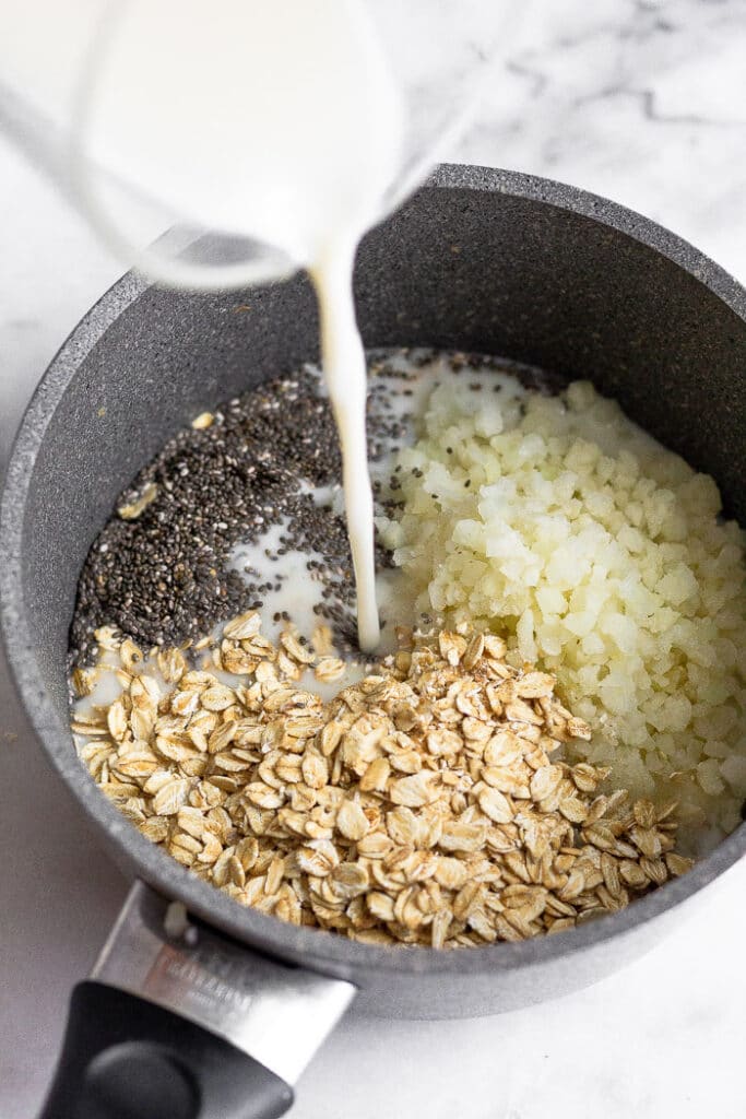 Saucepan with rolled oats, riced cauliflower, and chia seeds with milk bring poured in into it.
