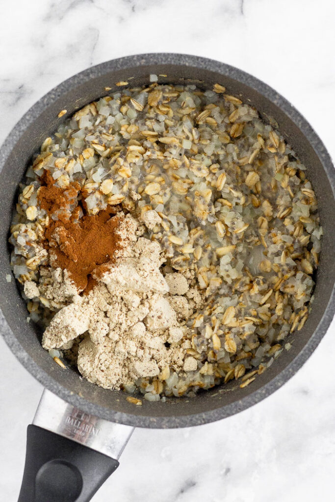 Cauliflower rice oatmeal in a saucepan with protein powder and cinnamon that will be stirred in.