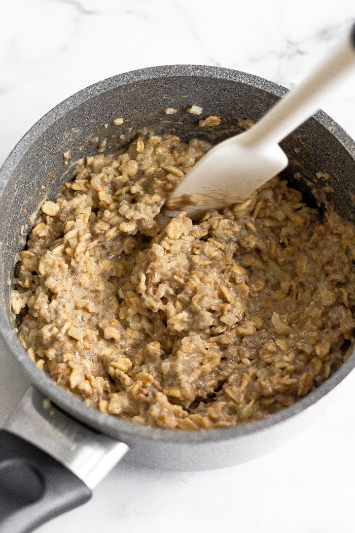 Saucepan filled with cauliflower oatmeal with a spatula stirring it.