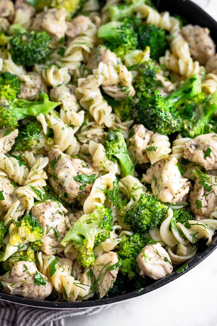 Close up of broccoli chicken pasta in a large pan with lots of fresh herbs mixed in.
