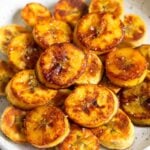 A pile of fried sweet plantains on a white plate. They are garnished with flaky salt.