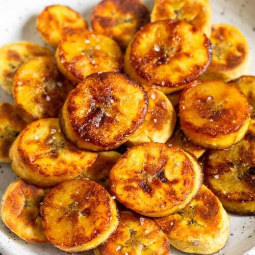 A pile of fried sweet plantains on a white plate. They are garnished with flaky salt.