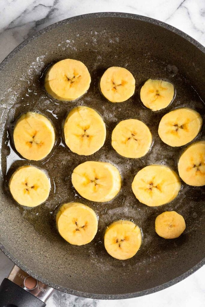 Overhead shot of a large skillet with plantains cooking in it.