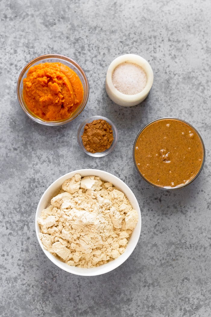 Overhead shot filled with a small of pumpkin puree, container of salt, bowl of almond butter, bowl of protein powder, and bowl of spices.