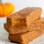 A stack of 3 pumpkin protein bars with a bite taken out of the first one. In the background is a small pumpkin.