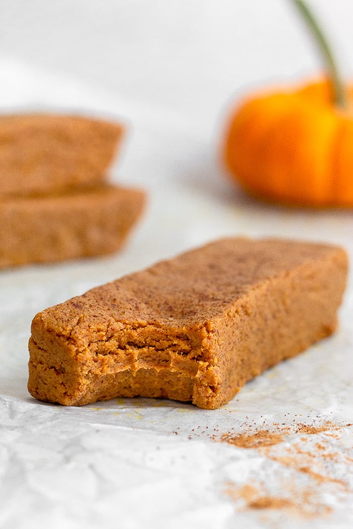 A homemade perfect bar pumpkin spice with a bite taken out of it. Behind it is two bars stacked on top with each other and a small pumpkin.