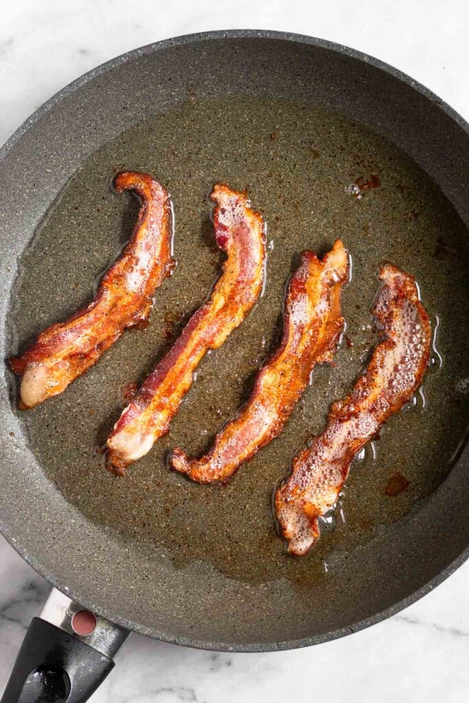 Four pieces of cooked bacon in a skillet.