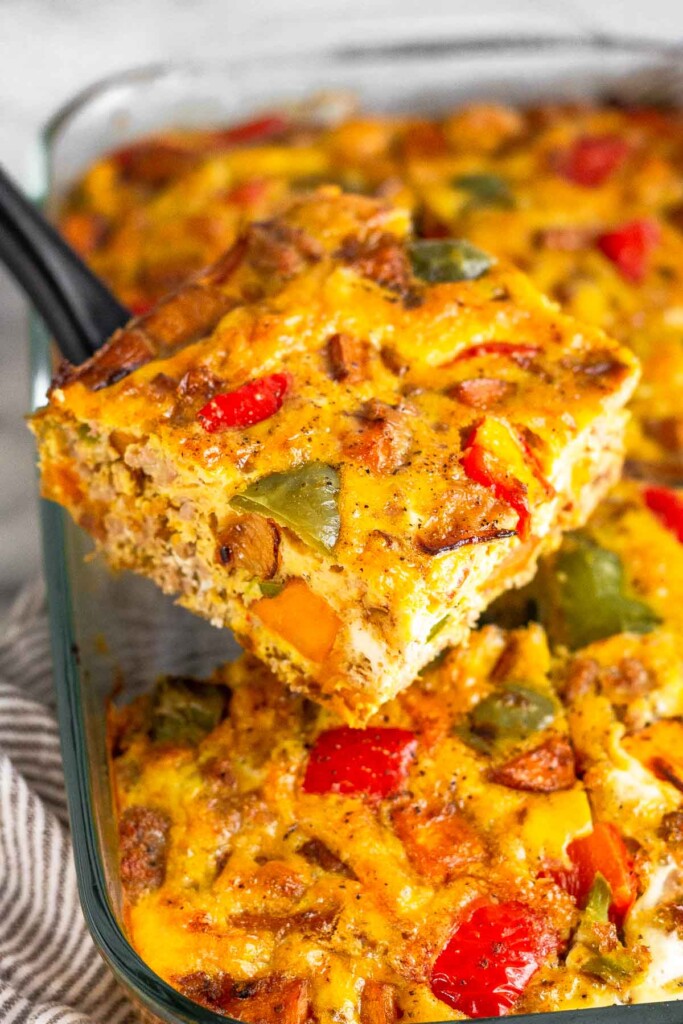 A piece of sausage potato breakfast casserole being held with a spatula over the plan of the rest of the casserole.