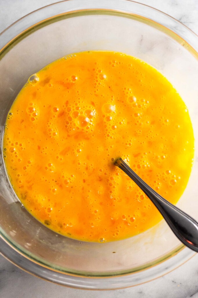 Large glass bowl with whisked eggs and a fork in it.