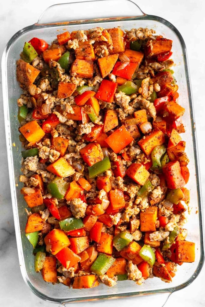 Overhead shot of a glass casserole dish filled with cooked ground sausage, sautéed diced sweet potatoes, peppers, and onions all mixed together.
