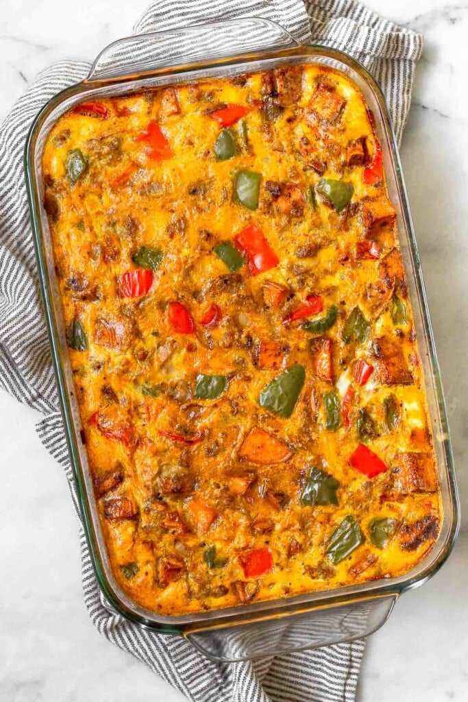 Overhead shot of sweet potato sausage breakfast casserole in a large casserole dish. The dish is sitting on top of a striped kitchen towel.