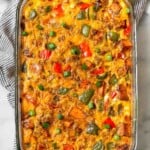 Sweet potato breakfast casserole with sausage and peppers in a large glass casserole dish. The dish is in a striped kitchen towel and next to is is a bowl of chopped green onions and half an avocado.