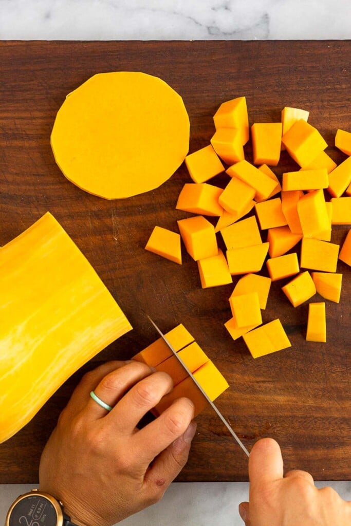 Overhead shot of someone dicing a butternut squash on a wooden cutting board.