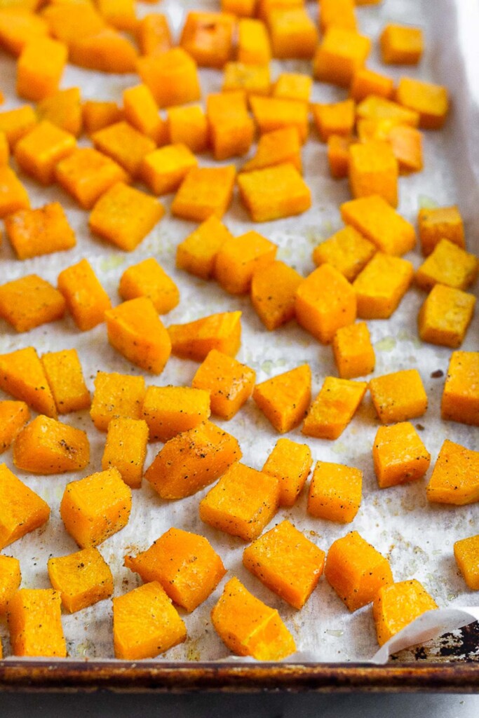 Roasted butternut squash cubes on a baking sheet lined with parchment paper.