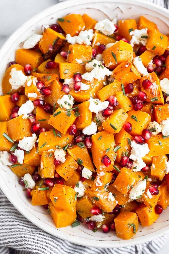 Roasted butternut squash with goat cheese and pomegranates tossed with a rosemary dressing in a large bowl.