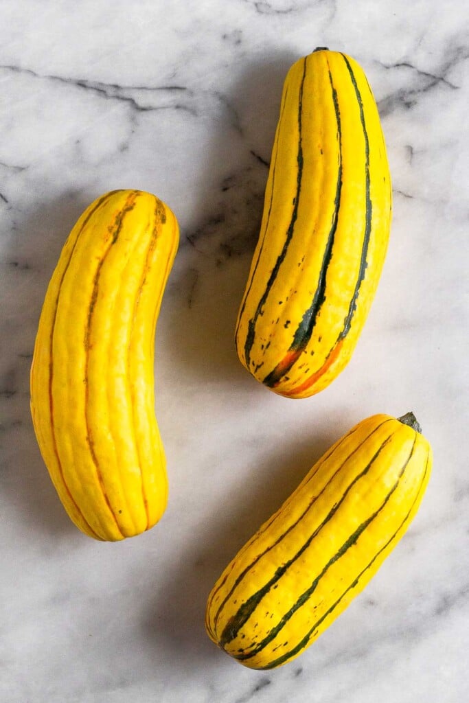 Three whole delicata squash on a white marble countertop.