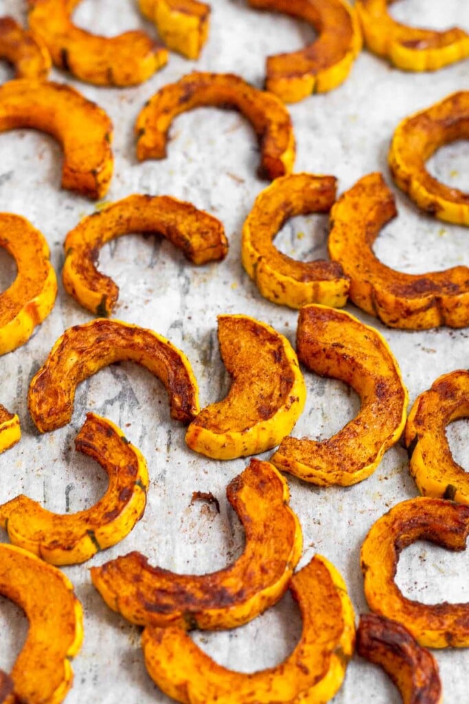 Pieces of baked delicata squash spread out on a baking sheet.