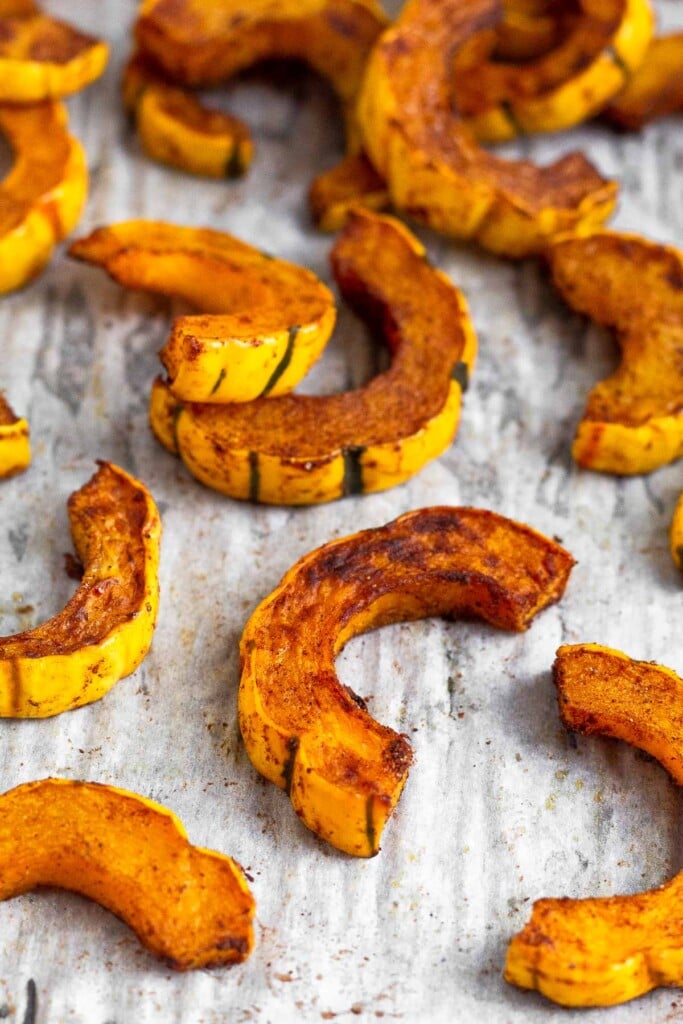 Half moon pieces of roasted delicata squash spread out on a on baking sheet.