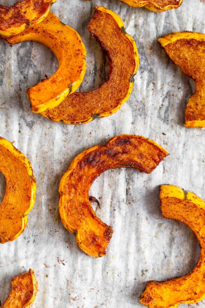 Overhead shot of half moon pieces of oven roasted delicata squash on baking sheet.