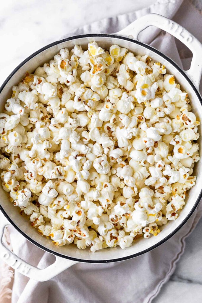 Large white dutch oven filled with freshly popped popcorn.