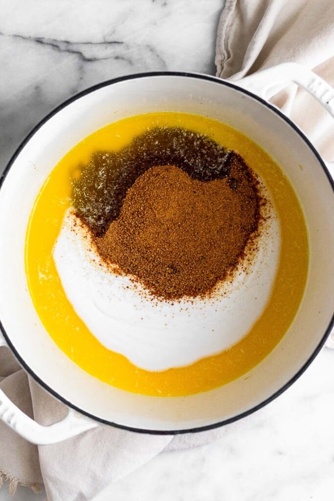 Large white dutch oven with melted butter, coconut milk, and coconut sugar in it.