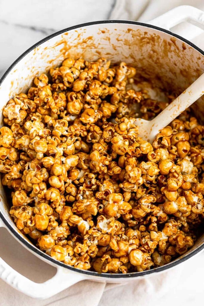 Large white dutch oven with popcorn being mixed with caramel sauce.