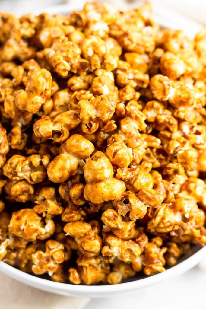 A close up shot of homemade caramel popcorn in a white bowl.