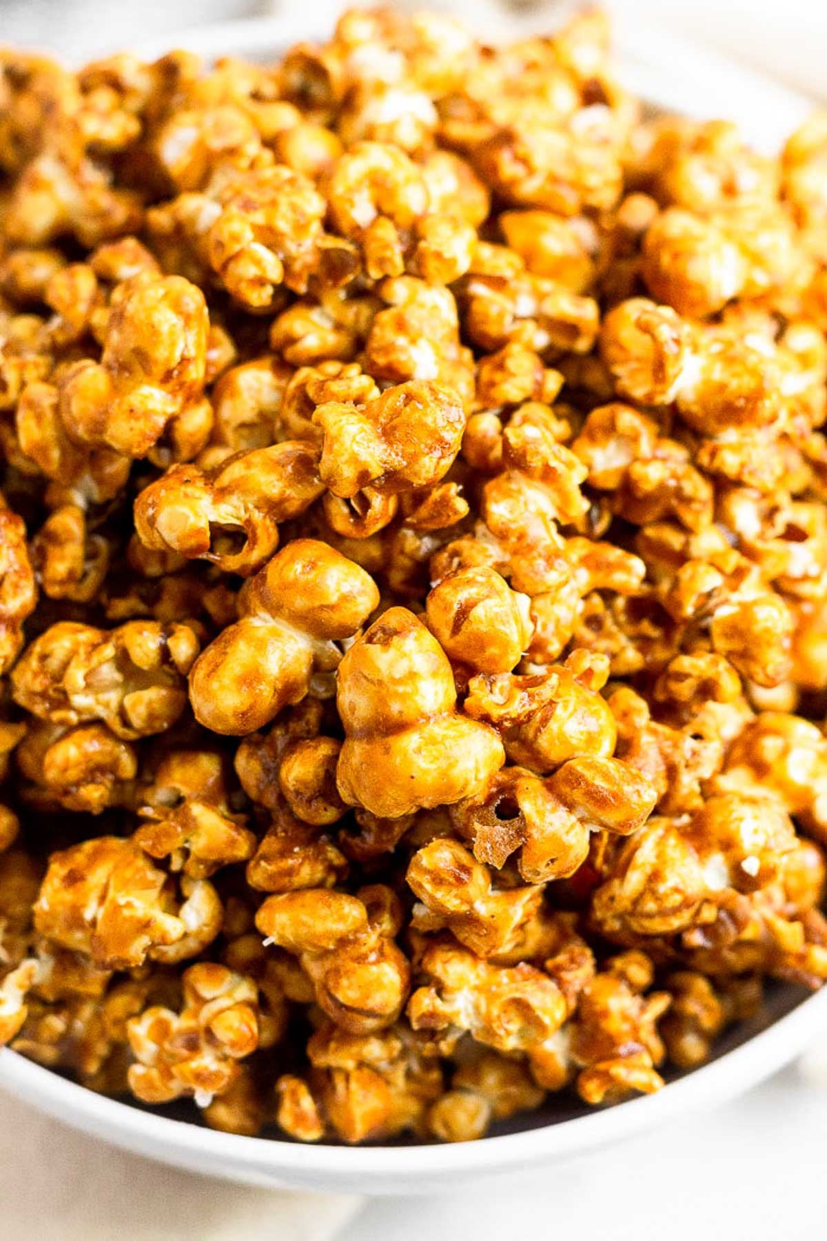 A close up shot of homemade caramel popcorn in a white bowl.