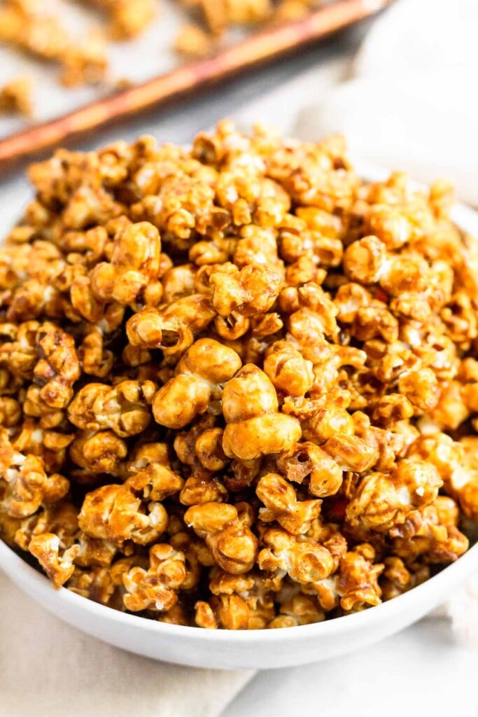 A big bowl of homemade caramel corn. Behind the bowl is a sheet pan with more caramel corn.