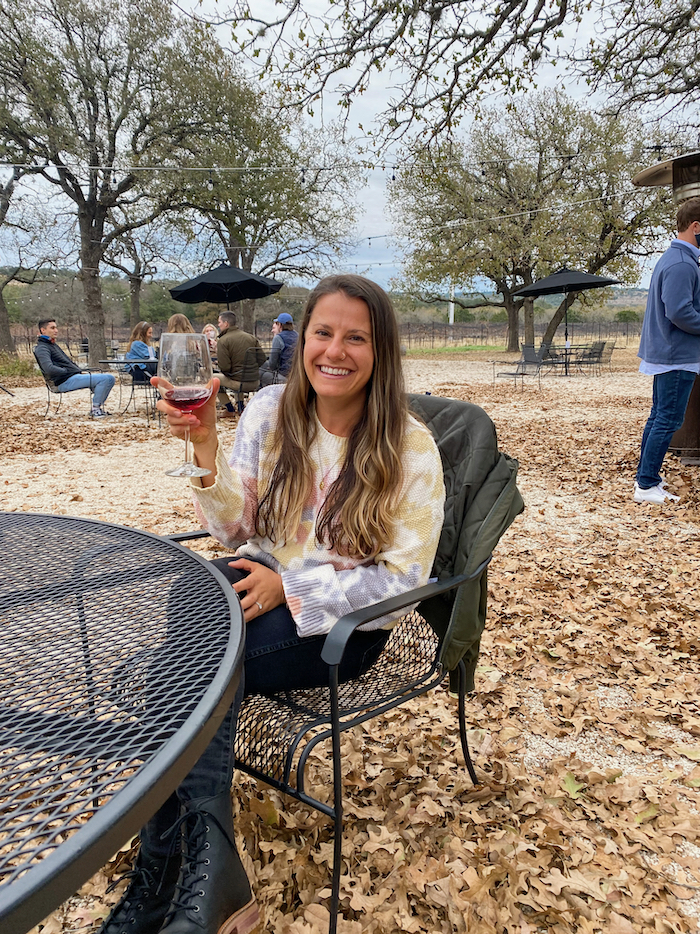 Woman sitting at a table outside smiling holding a glass of wine.