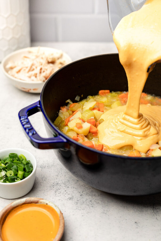 A pot of soup with a thick broth being poured into it. Around it is a bowl of hot sauce, a bowl of green onions, and a bowl of shredded chicken.