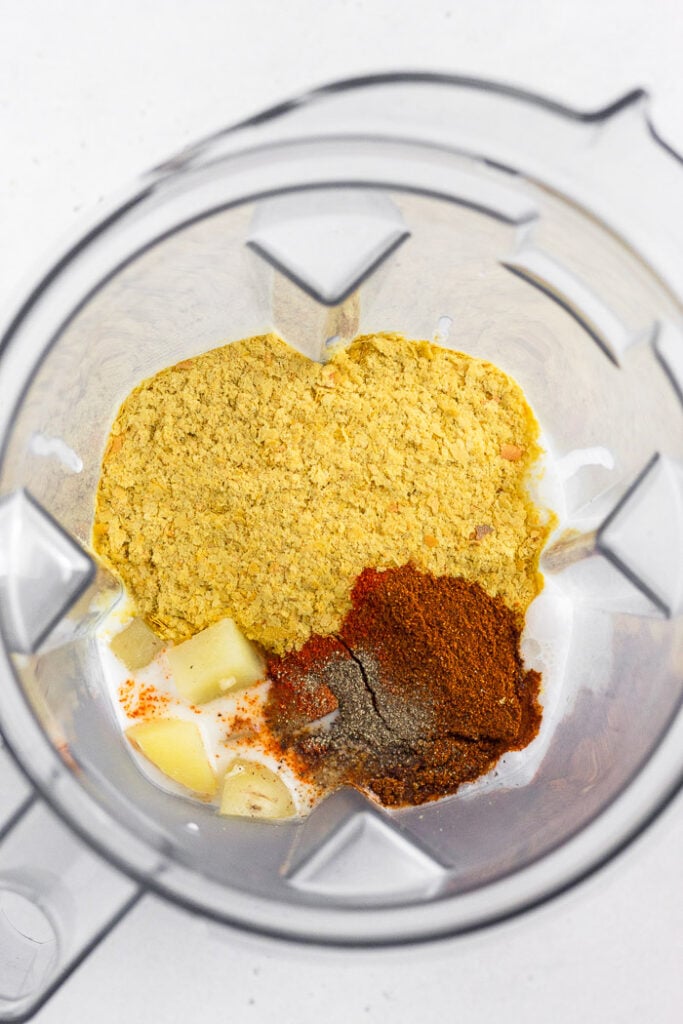 Blender filled with coconut milk, potatoes, nutritional yeast, and spices.