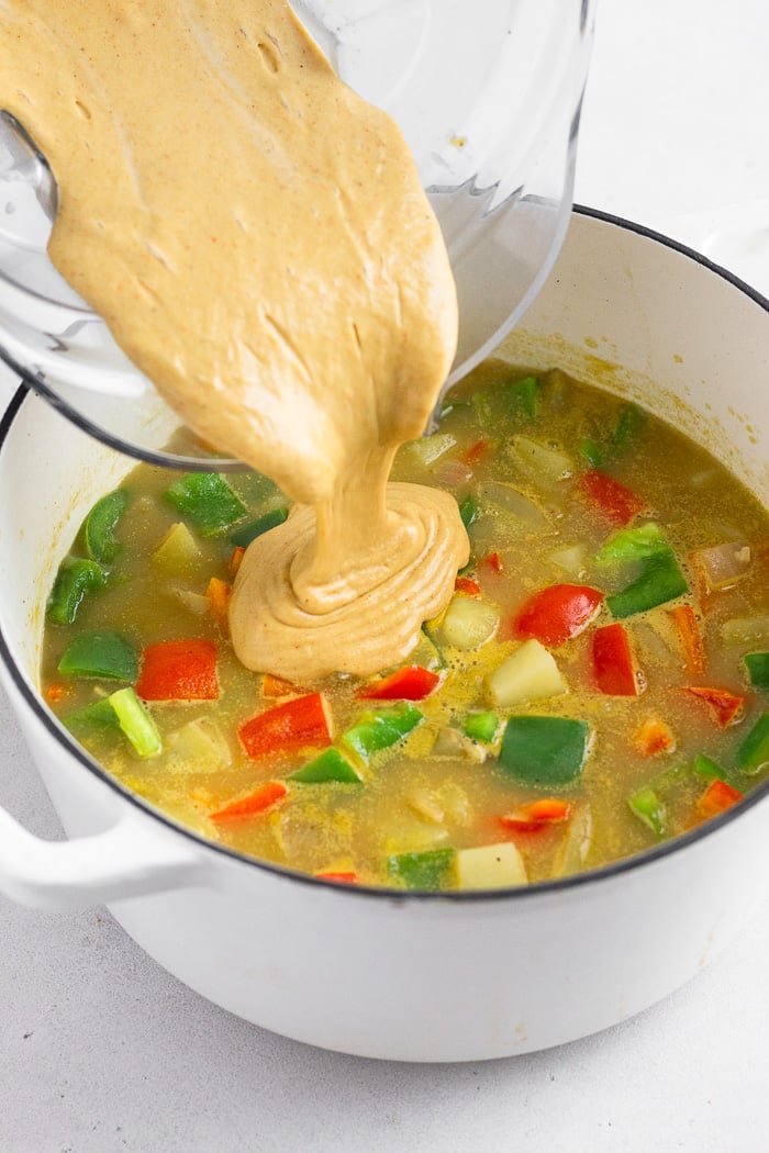 Large stockpot filled with soup with a creamy thick broth being poured into it.