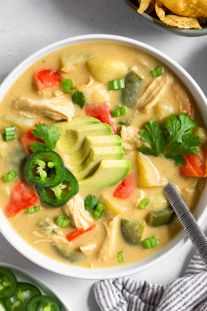 A bowl of cheesy chicken potato soup topped with avocado, jalapeños, cilantro, and green onions.
