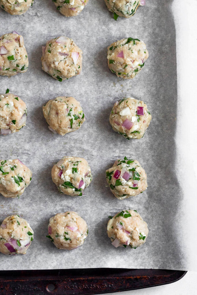 Baking sheet lined with parchment paper with chicken meatballs on them before they are baked.