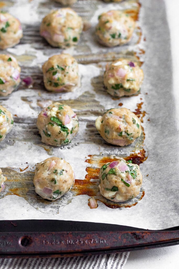 Baked greek chicken meatballs on a baking sheet lined with parchment paper.
