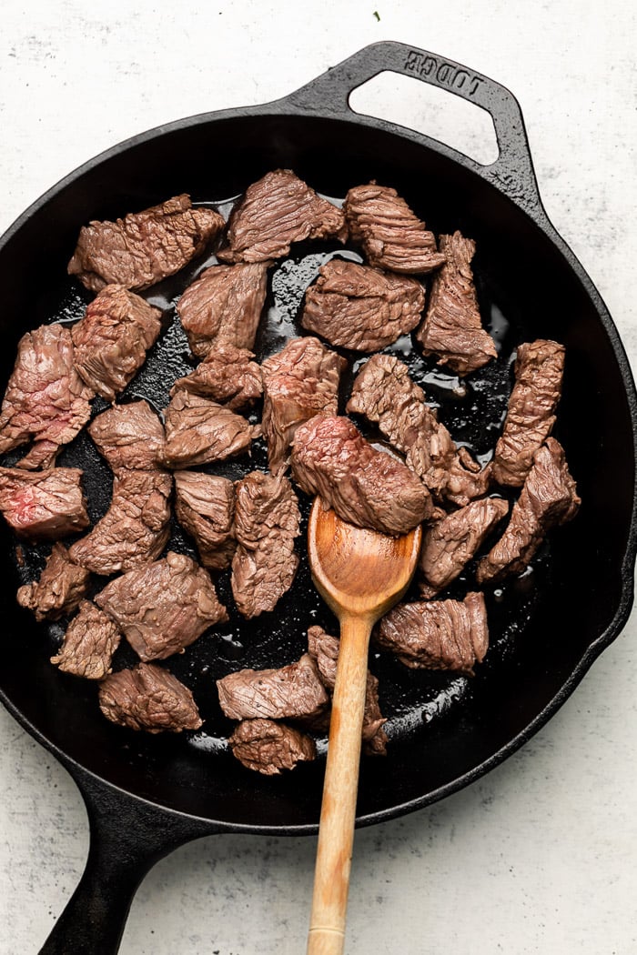 Pan filled with steak bites with a wooden spoon.