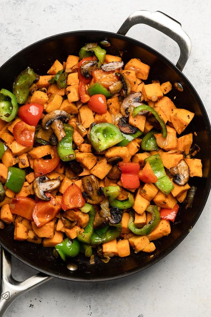 Large pan filled with diced sweet potatoes, peppers, and mushrooms.