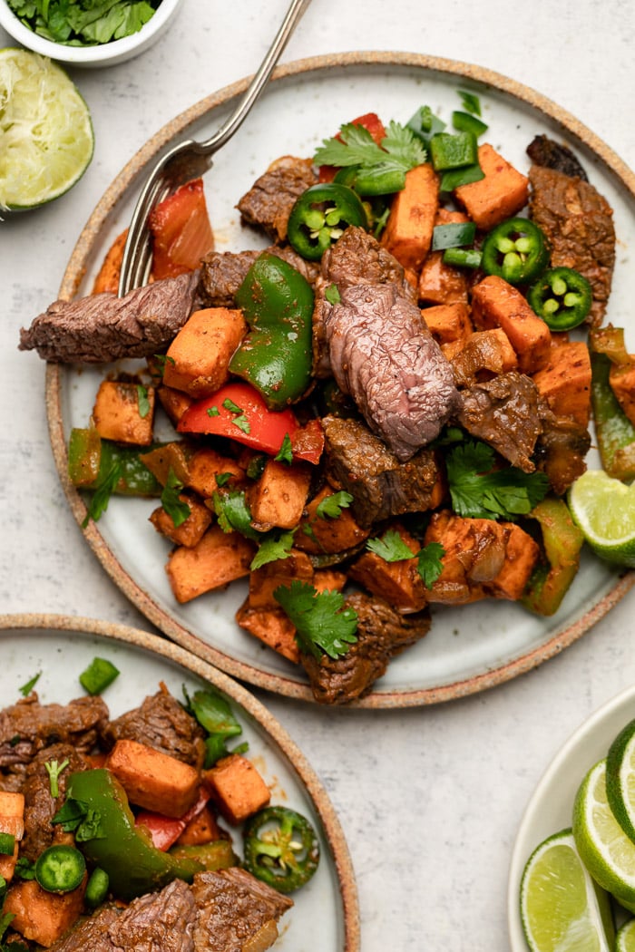 Two plates with steak and sweet potatoes garnished with cilantro and jalapeños.