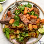 Plate with steak and sweet potato topped with cilantro and jalapeños. Next to it is a stripped towel, lime wedge, and a bowl of cilantro.