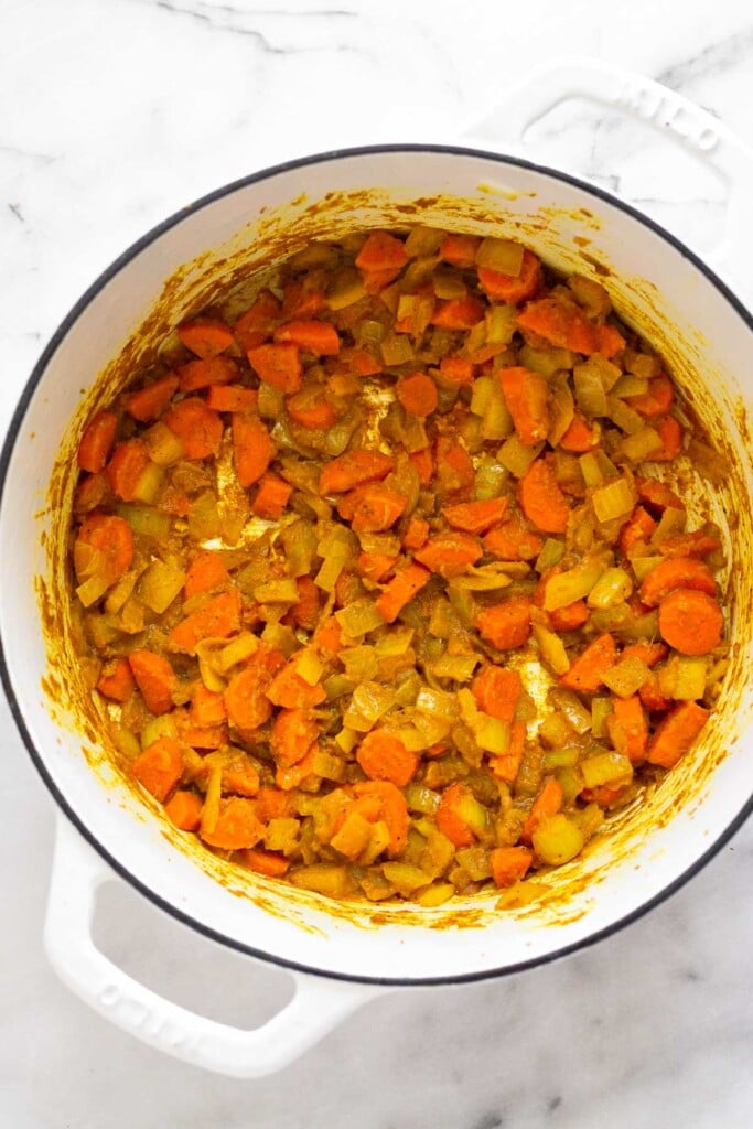 A mixture of sautéed carrots, onions, and spices in a white dutch oven.