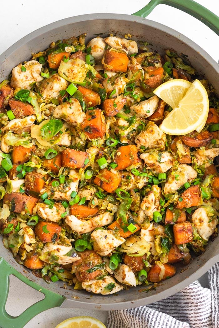 A pan of maple mustard chicken skillet with sweet potatoes and Brussels with lemon wedges on top.