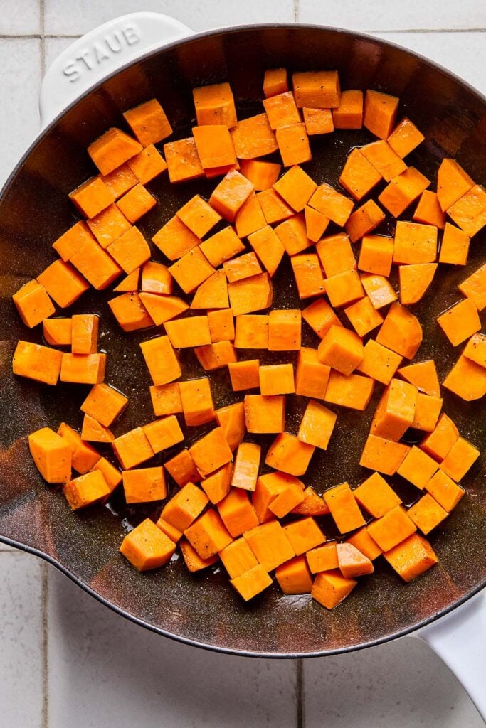 Large enameled skillet filled with sautéed diced sweet potatoes.