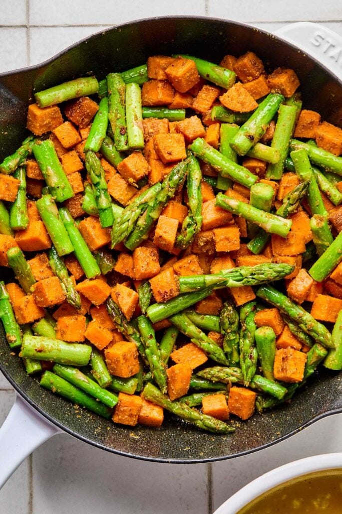 Large enameled skillet filled with sautéed diced sweet potatoes and chopped asparagus.